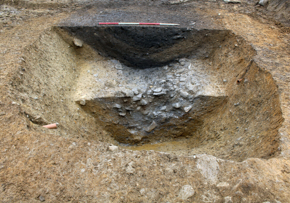 Slot through the enclosure ditch, showing stones tumbled from the bank into the cut, with distinct fills visible above.